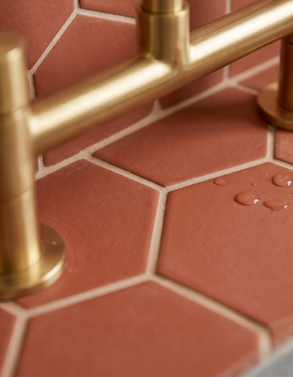 Terracotta hexagonal tiles by Clay Imports with white grout, a brass fixture, and water droplets.