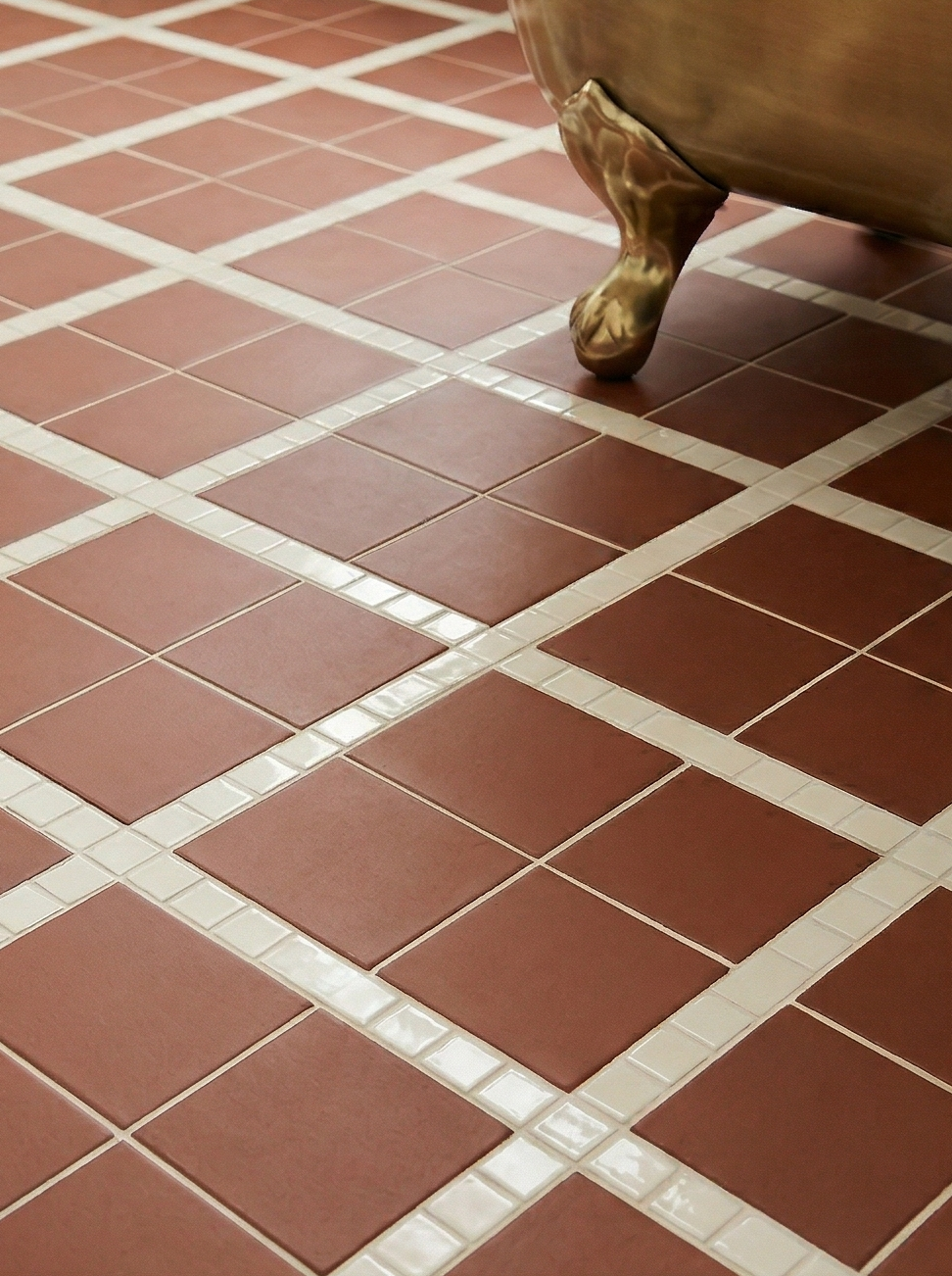 Mamey reddish-brown clay tile by Clay Imports, in a diamond pattern with white mosaic strips on a bathroom floor, beside a brass tub leg.