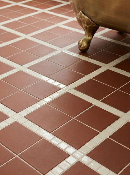 Mamey reddish-brown clay tile by Clay Imports, in a diamond pattern with white mosaic strips on a bathroom floor, beside a brass tub leg.
