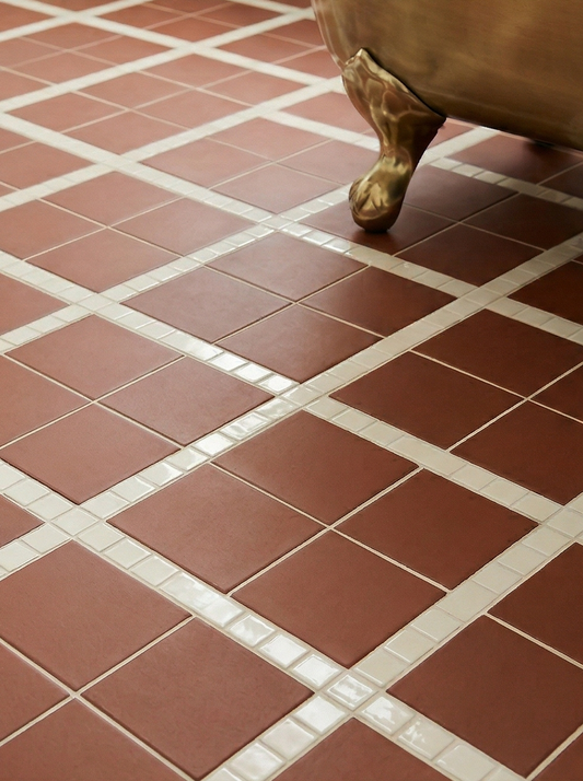 Mamey reddish-brown clay tile by Clay Imports, in a diamond pattern with white mosaic strips on a bathroom floor, beside a brass tub leg.