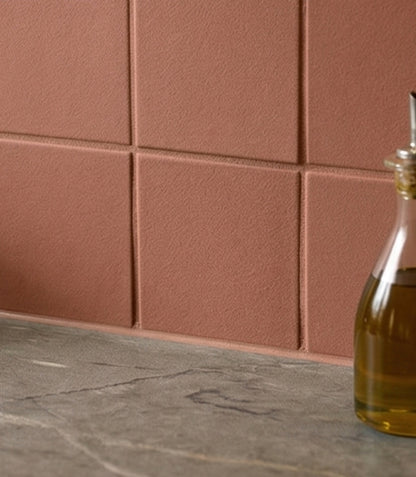 Dusky red textured square clay tiles by Clay Imports forming a backsplash over a dark countertop.