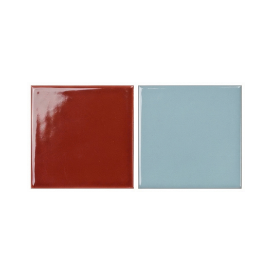 Two glossy ceramic square tiles sit side-by-side, showcasing a contrasting pair of rich terracotta red and soft pastel blue glazed finishes.
