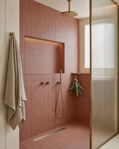Pink square clay tiles by Clay Imports in a shower with bronze fixtures and a lighted wall niche.