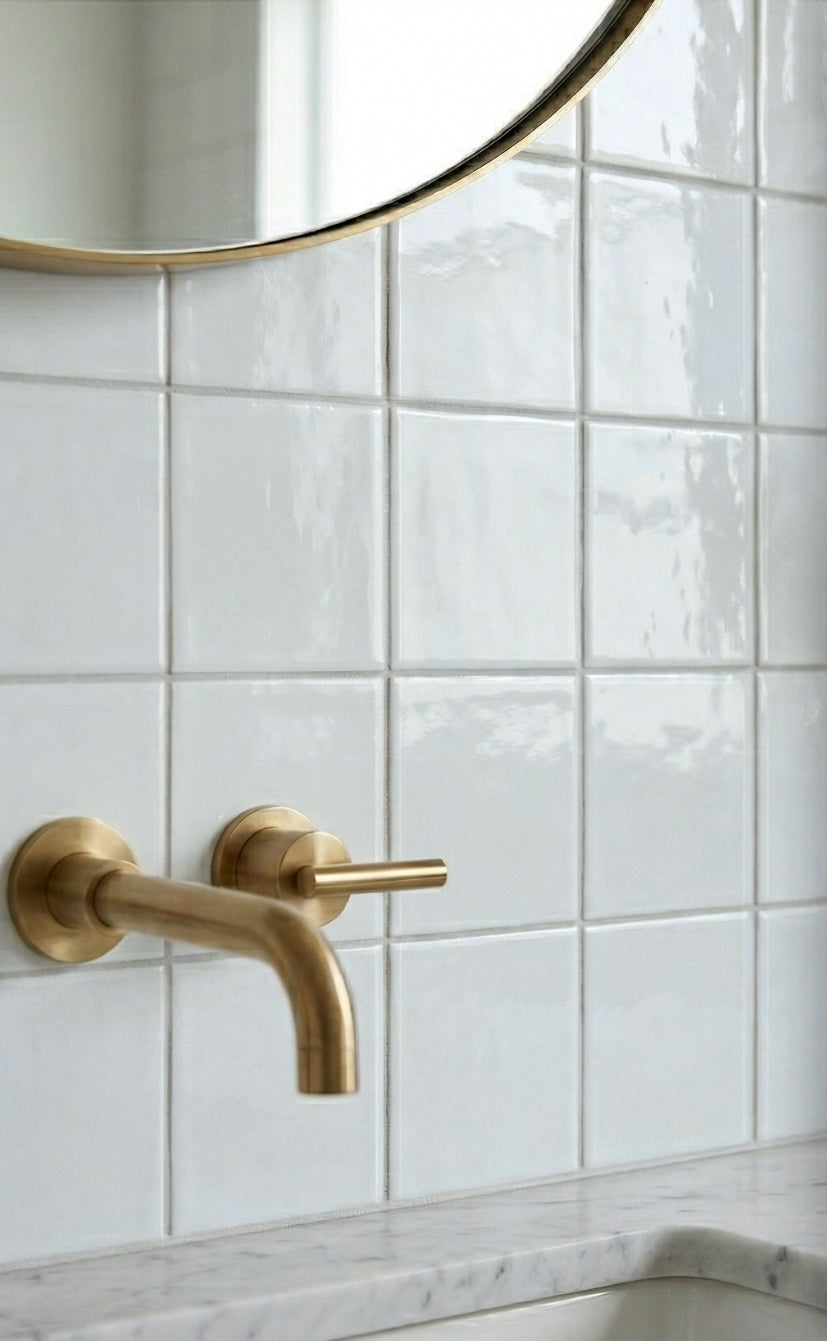 Spearmint solid tile by Clay Imports, featuring glossy square tiles, a brass faucet, and a round mirror.