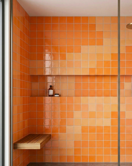 Orange square clay tiles by Clay Imports with a subtle color gradient, integrated niche, and wooden bench in a modern shower.