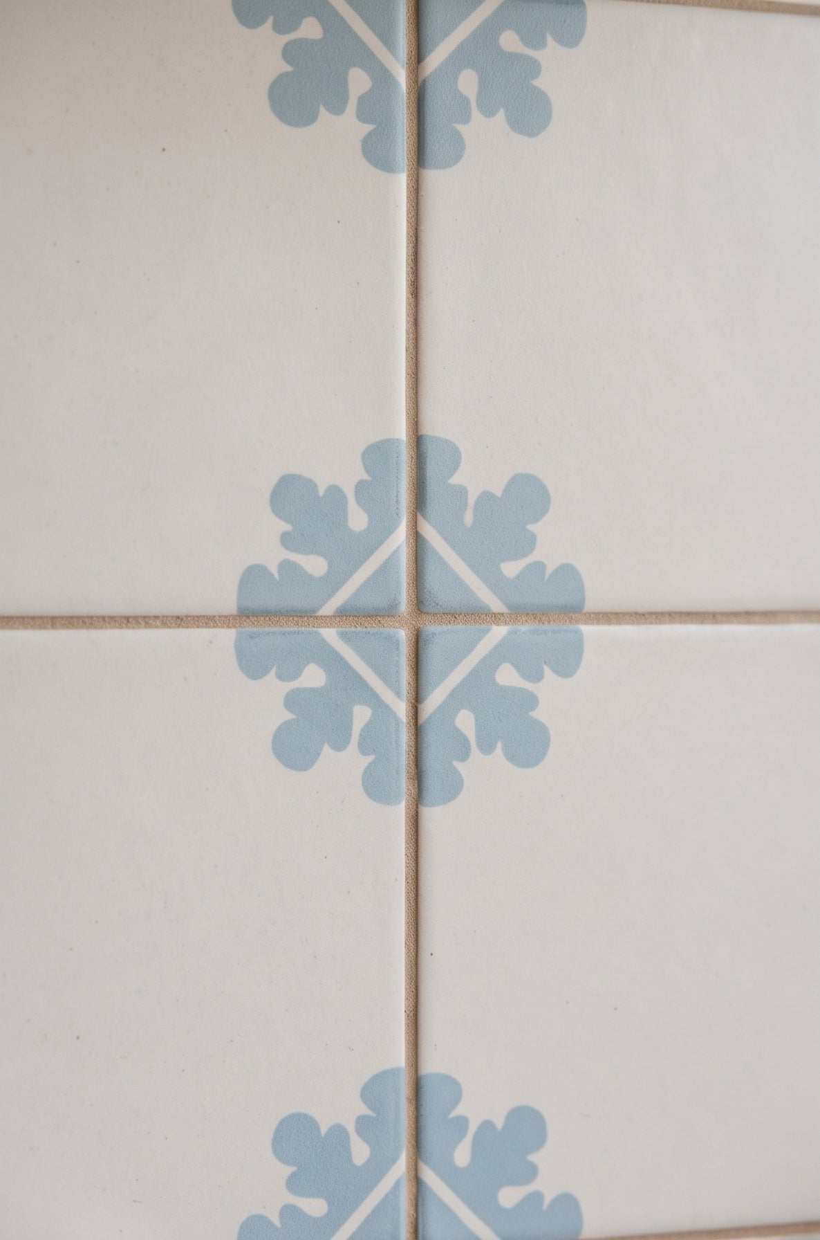 White Talavera tile with light blue floral motif by Clay Imports, arranged in grid with beige grout, close-up view