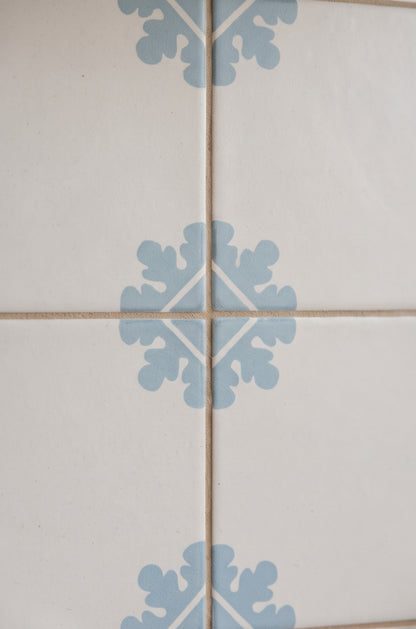 White Talavera tile with light blue floral motif by Clay Imports, arranged in grid with beige grout, close-up view