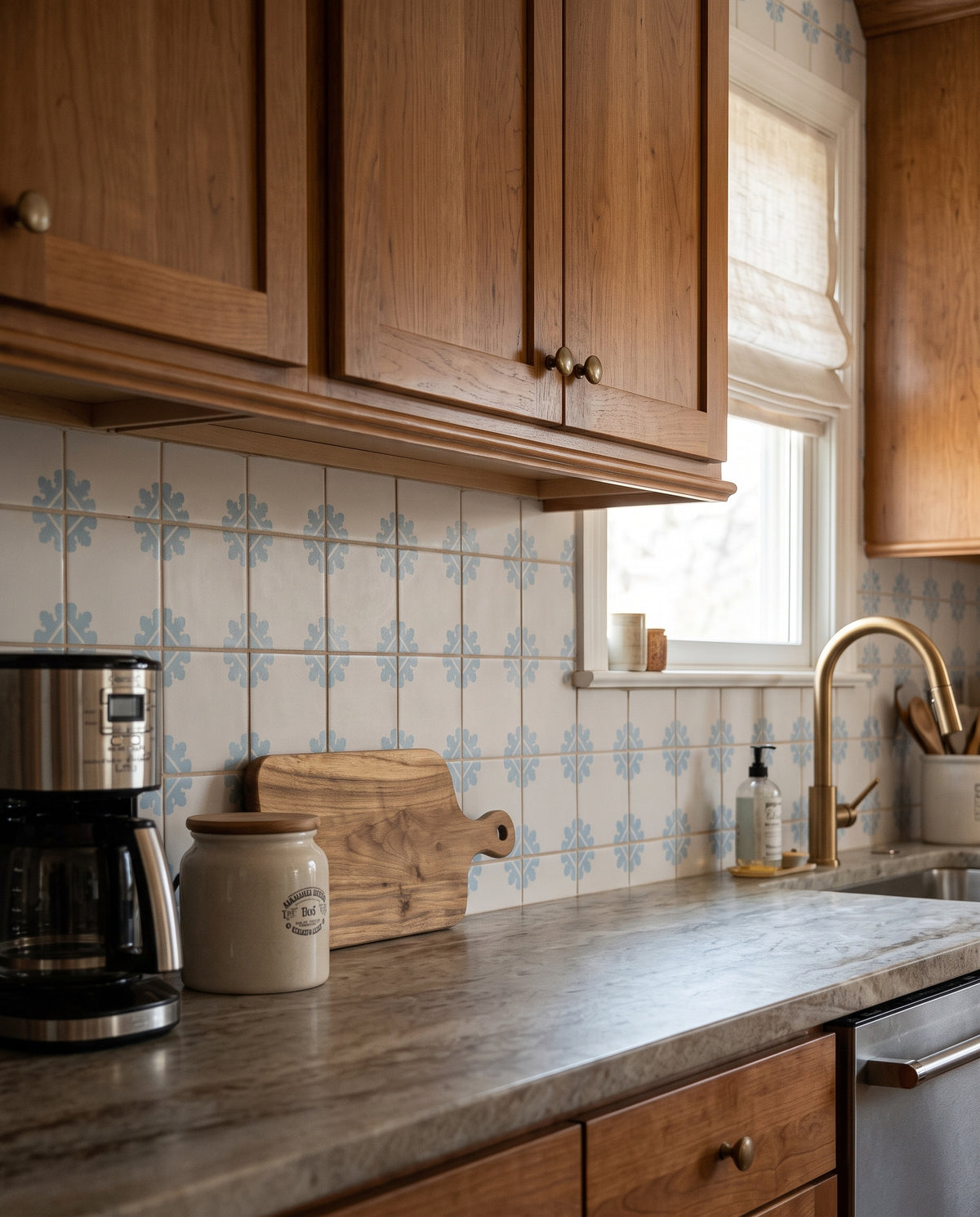 Creamy white Talavera tile with blue floral pattern by Clay Imports, installed as kitchen backsplash with wooden cabinetry and marble countertop.