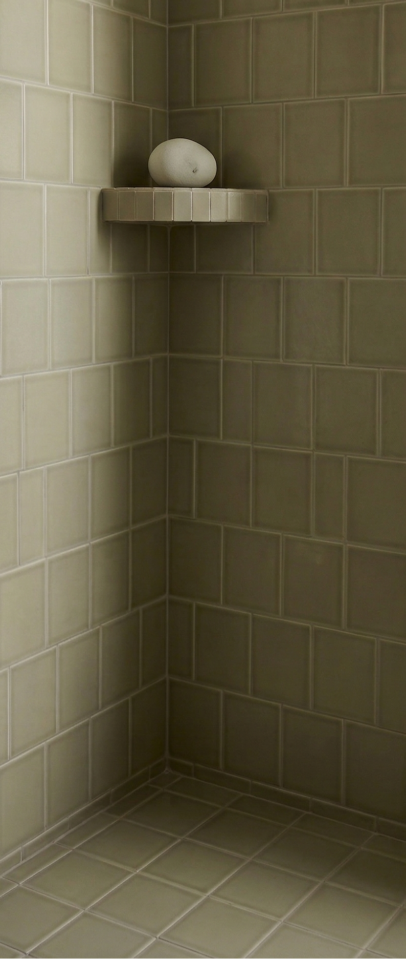 Yucca green rectangular solid tile by Clay Imports, with a crackle gloss finish, installed in a shower corner, featuring a shelf and white oval stone.