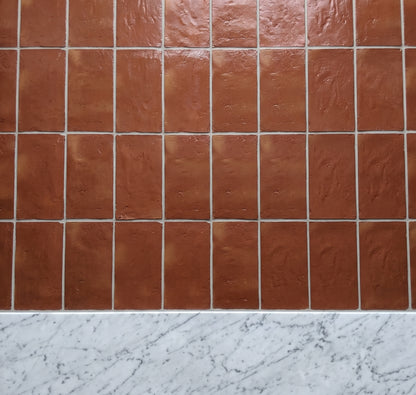 Terracotta brown square ceramic tiles arranged in a grid pattern with a white marble countertop visible at the bottom.