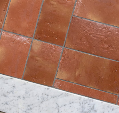 Terracotta brown rectangular stone-look tiles arranged in a herringbone pattern, shown with a white marble countertop edge.