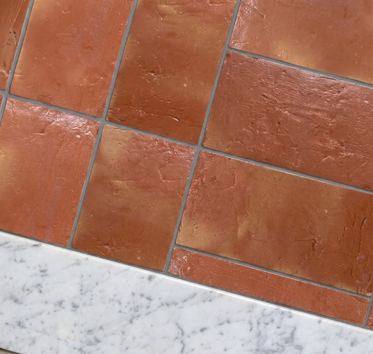 Terracotta brown rectangular stone-look tiles arranged in a herringbone pattern, shown with a white marble countertop edge.