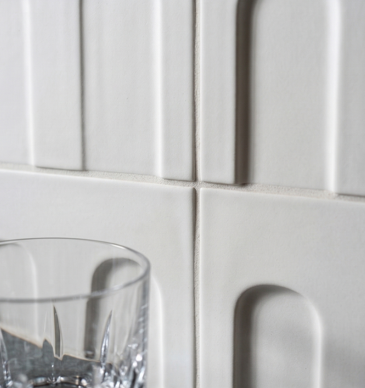 Chalk white clay tiles by Clay Imports with embossed vertical and arched patterns; cropped with a glass.