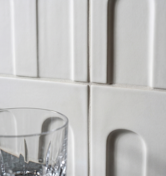 Chalk white clay tiles by Clay Imports with embossed vertical and arched patterns; cropped with a glass.