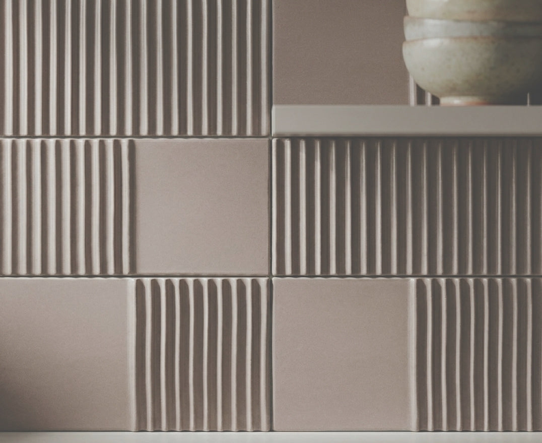 Textured brown clay tiles by Clay Imports, arranged in a grid with smooth and vertically ribbed sections, below stacked bowls.