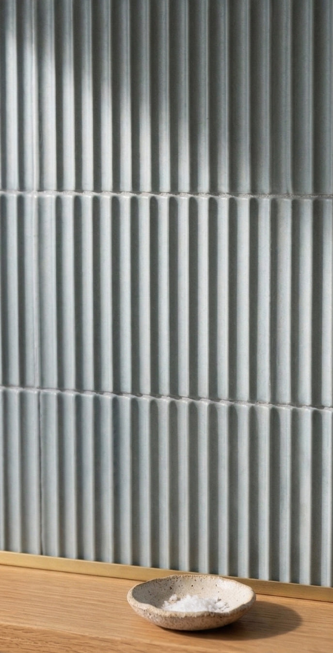 Zurco pale green ridged clay tiles by Clay Imports, installed as a wall with a small bowl of salt on a wooden counter.