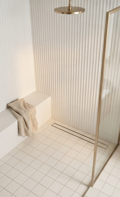 Cream-colored square solid tile in a modern shower floor, featuring a matte finish and subtle grid layout, with ribbed wall tiles and gold fixtures.
