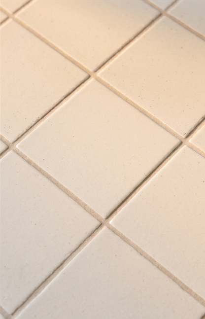 Cream-colored square solid tile with subtle speckled texture and light grout, arranged in diagonal grid pattern, close-up view