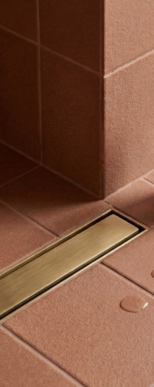 Lava Rock Matte 4x5 solid tile by Clay Imports, in a shower setting with a textured reddish-brown finish and a bronze linear drain.