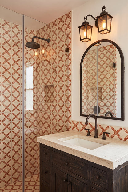 A modern bathroom features a dark wood vanity with a marble countertop, an arched mirror, and a walk-in shower lined with terracotta-patterned tiles.