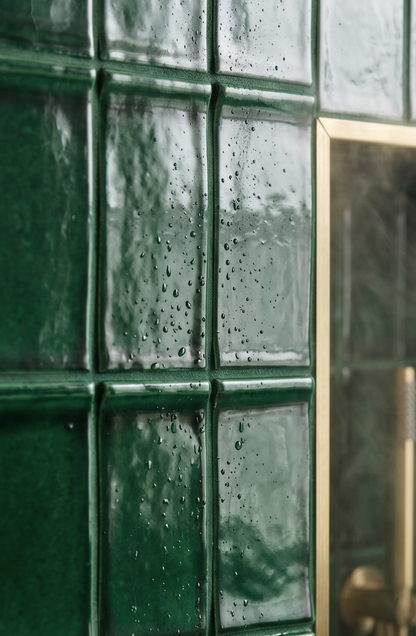 Green glossy rectangular tiles by Clay Imports with visible water droplets on a textured surface and a gold trim.