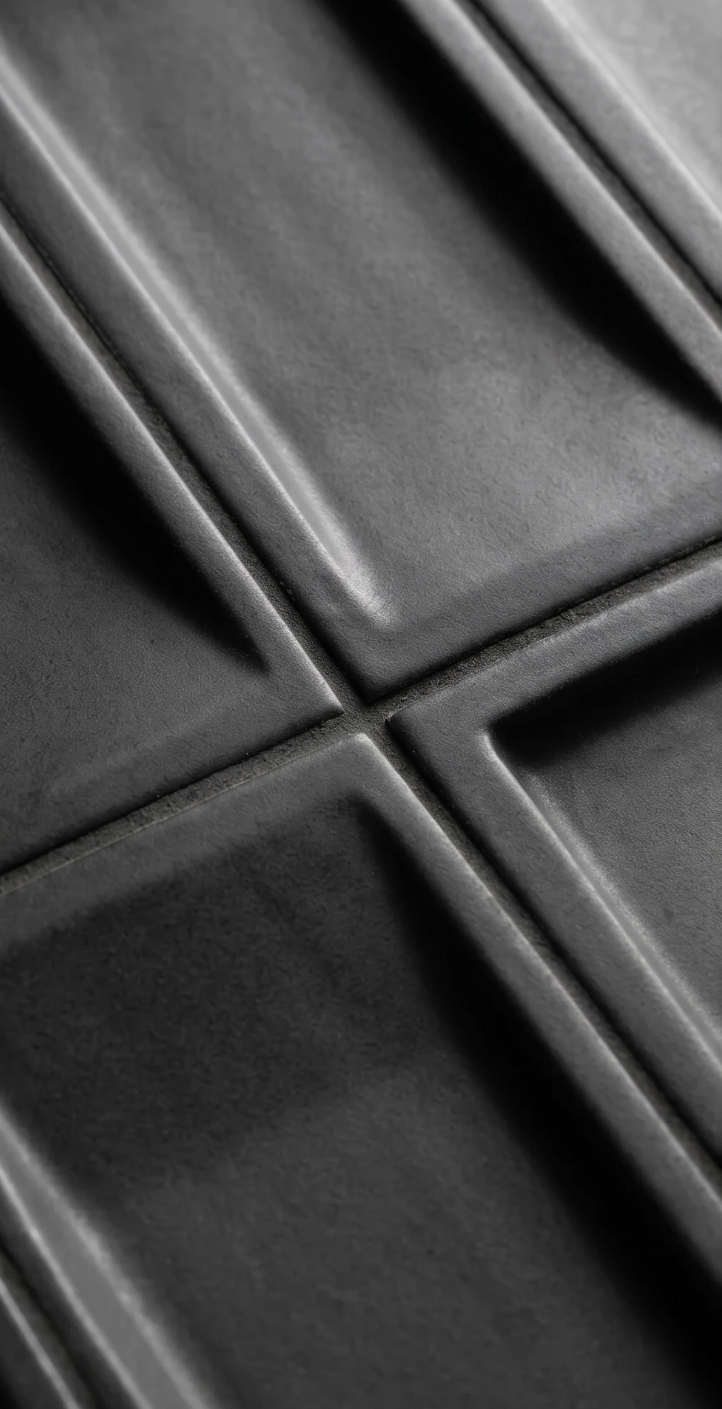 Dark matte black geometric relief tile by Clay Imports, showing raised square patterns and visible grout lines.