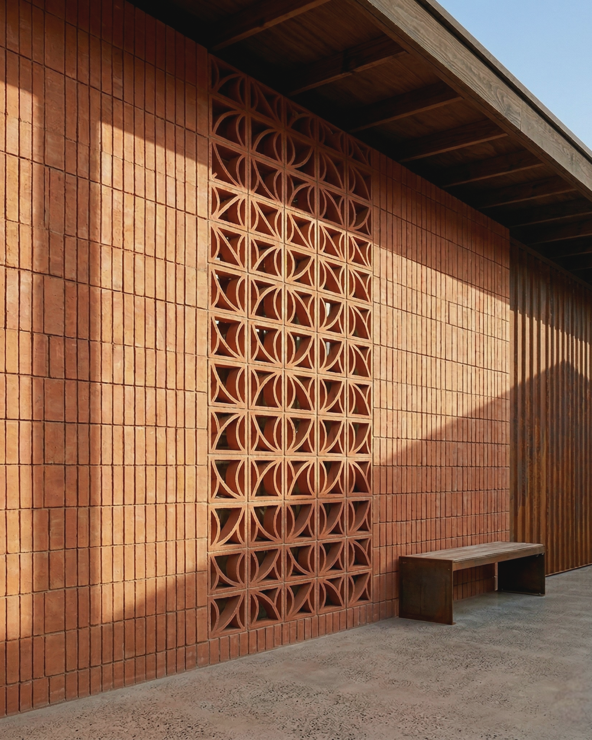 Terracotta Brisa breeze block by Clay Imports Breeze Blocks, featuring a repeating circular pattern as part of a wall with vertical bricks and a wooden bench.