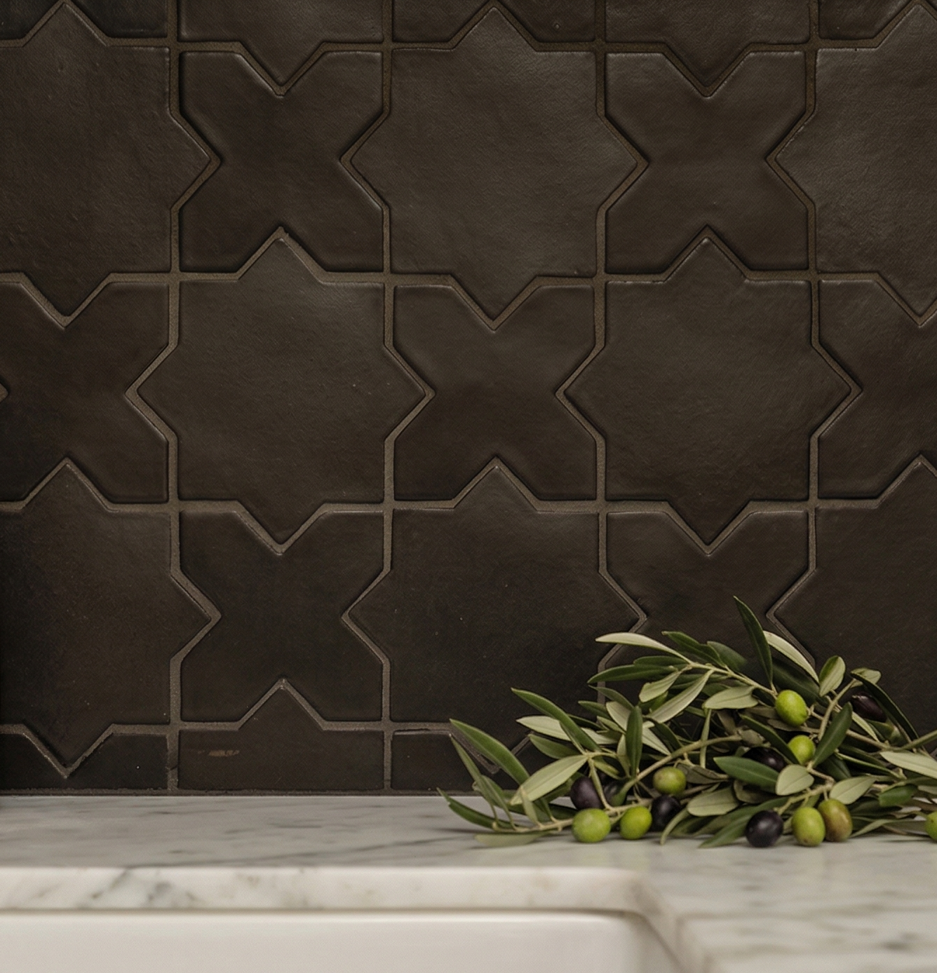 Black suede tile with Star & Cross pattern by Clay Imports, installed as a backsplash over a white marble counter with olive branches.