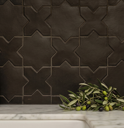 Black suede tile with Star & Cross pattern by Clay Imports, installed as a backsplash over a white marble counter with olive branches.