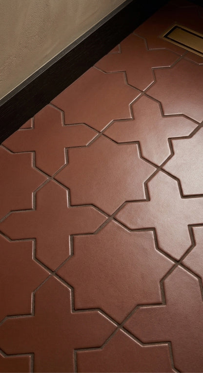 Cacao solid tile by Clay Imports with a textured star and cross pattern on a floor, next to dark trim.