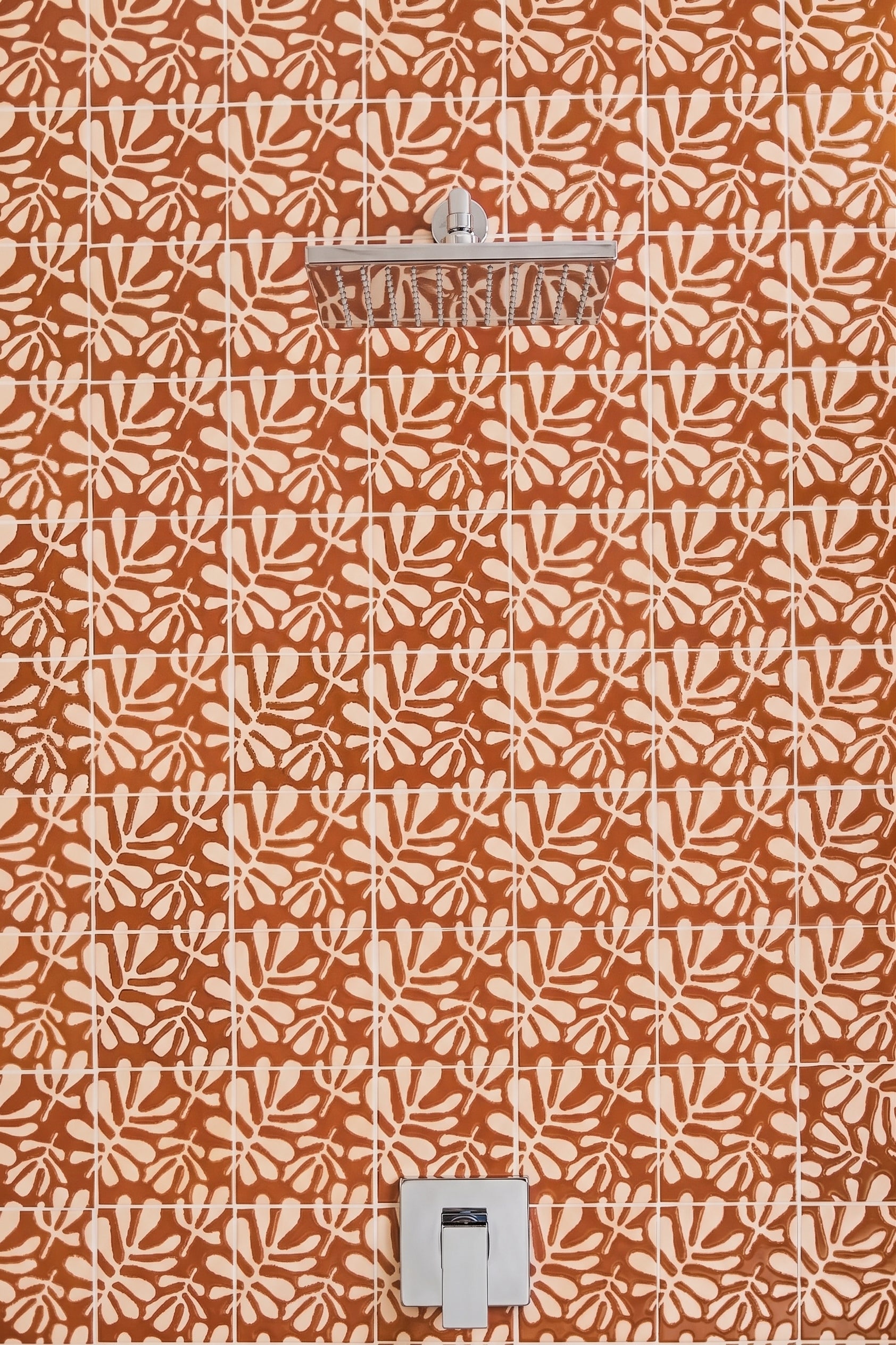 Terracotta orange and cream patterned wall tiles with a matching leaf motif, featuring a chrome shower head and a white wall-mounted control valve.
