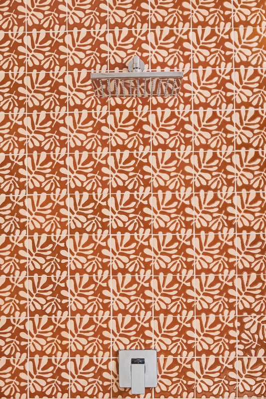 Terracotta orange and cream patterned wall tiles with a matching leaf motif, featuring a chrome shower head and a white wall-mounted control valve.