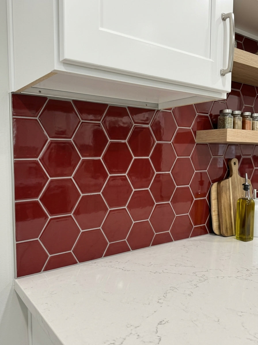 Red glossy hexagonal tile backsplash installed under white kitchen cabinets, with a white marble countertop and wooden cutting board on the right.