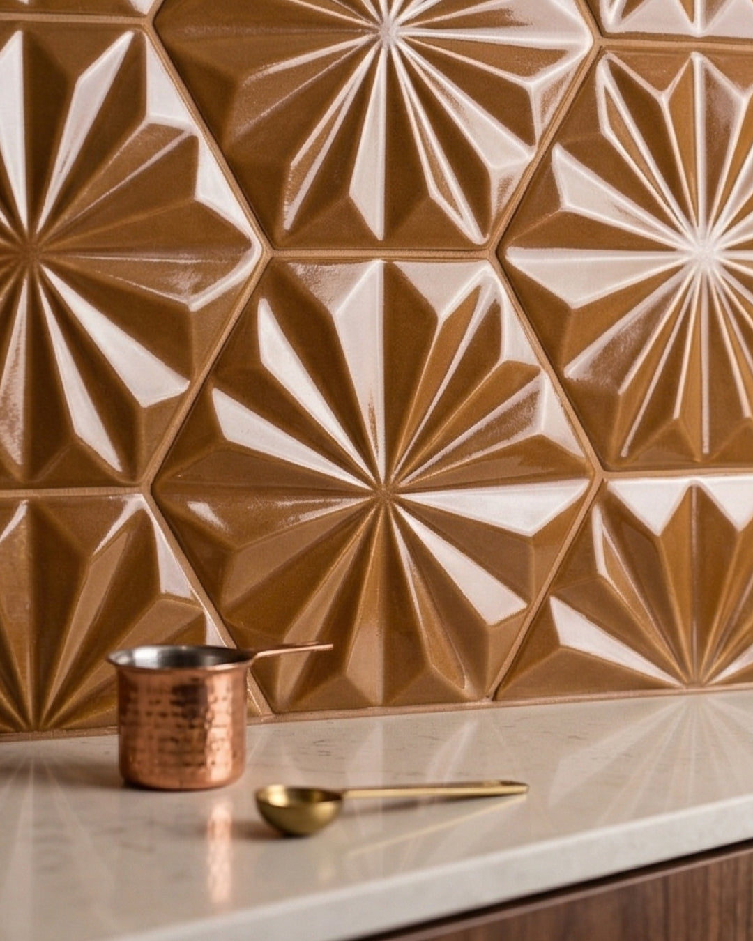 Caramel brown hexagonal solid tile by Clay Imports with a glossy 3D geometric sunburst pattern, on a countertop with a copper pot and golden spoon.
