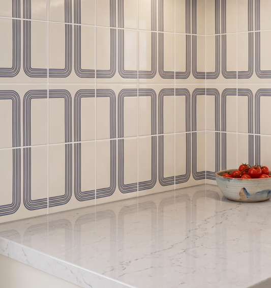 Tiled wall with geometric pattern and a bowl of tomatoes on a marble countertop.