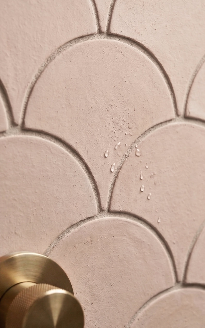 Pink scallop tiles by Clay Imports, matte with water droplets and a brass faucet handle.