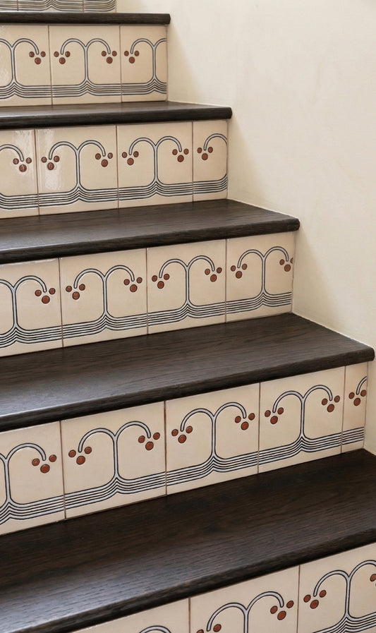 Cream pattern tile from Clay Imports with a repeating curvilinear wave and berry-like dot design on stair risers, alongside dark wood treads.