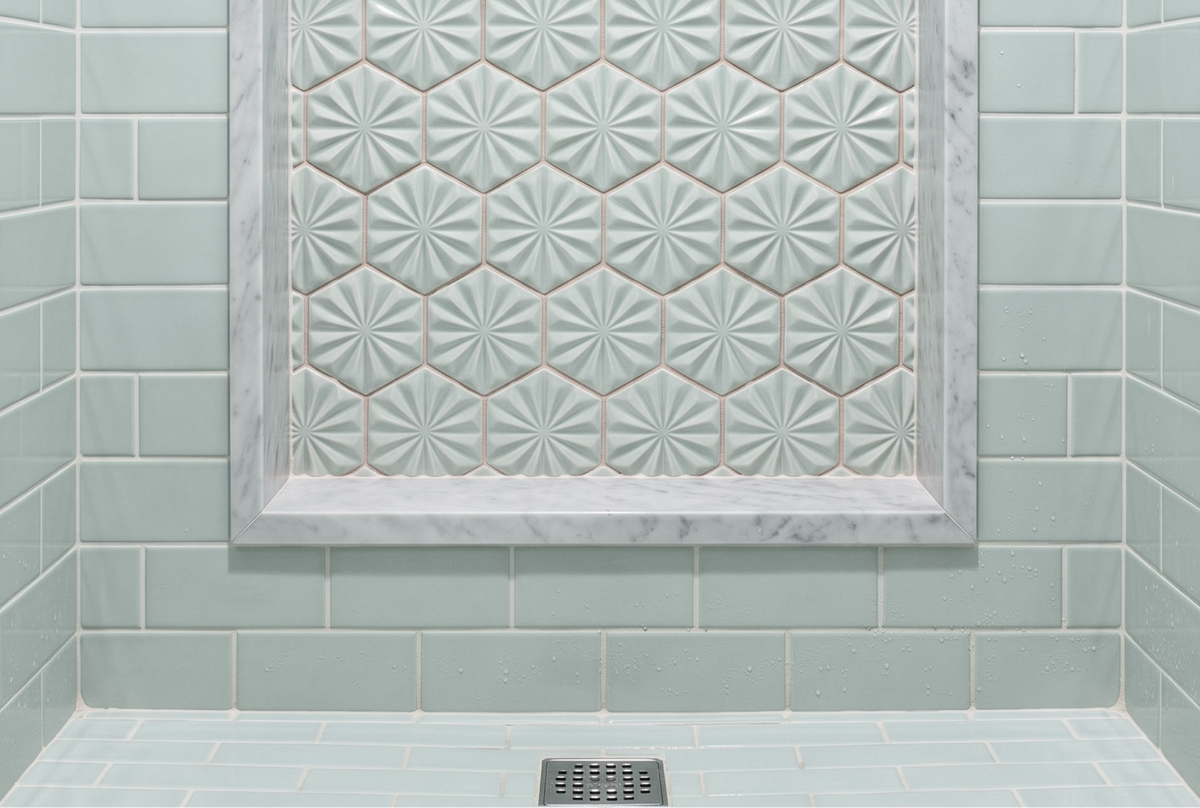 A modern shower features glossy light blue subway tiles on the walls and floor, complemented by a recessed shower niche lined with decorative starburst hexagonal tiles and framed in white marble.