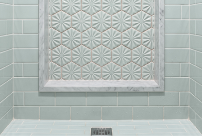 A modern shower features glossy light blue subway tiles on the walls and floor, complemented by a recessed shower niche lined with decorative starburst hexagonal tiles and framed in white marble.