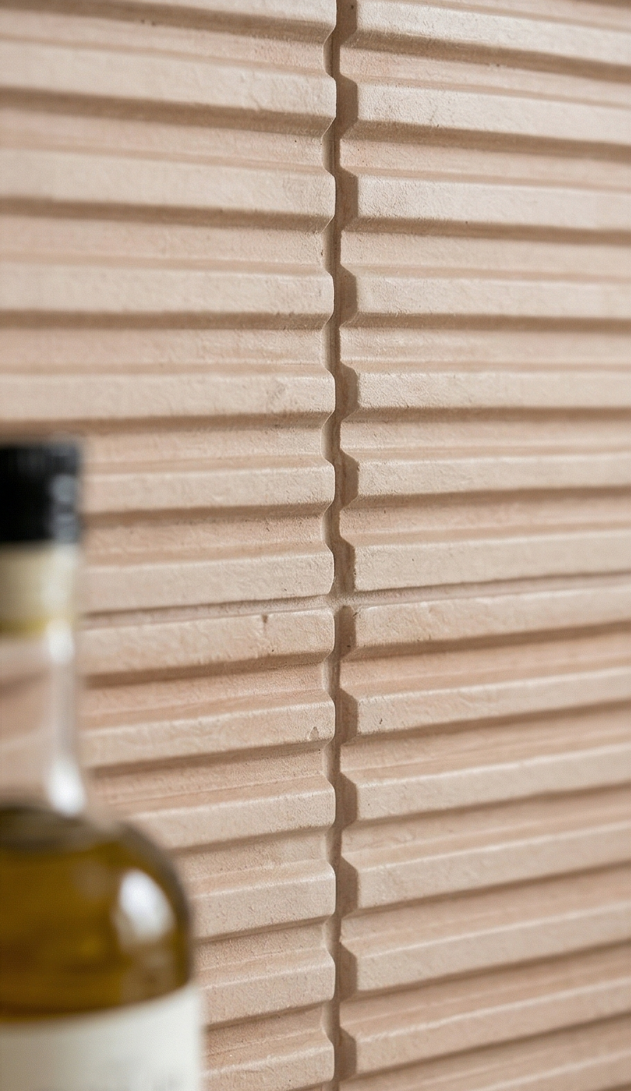 Light beige clay tile by Clay Imports with a horizontal corrugated pattern and visible texture, with a blurred bottle.