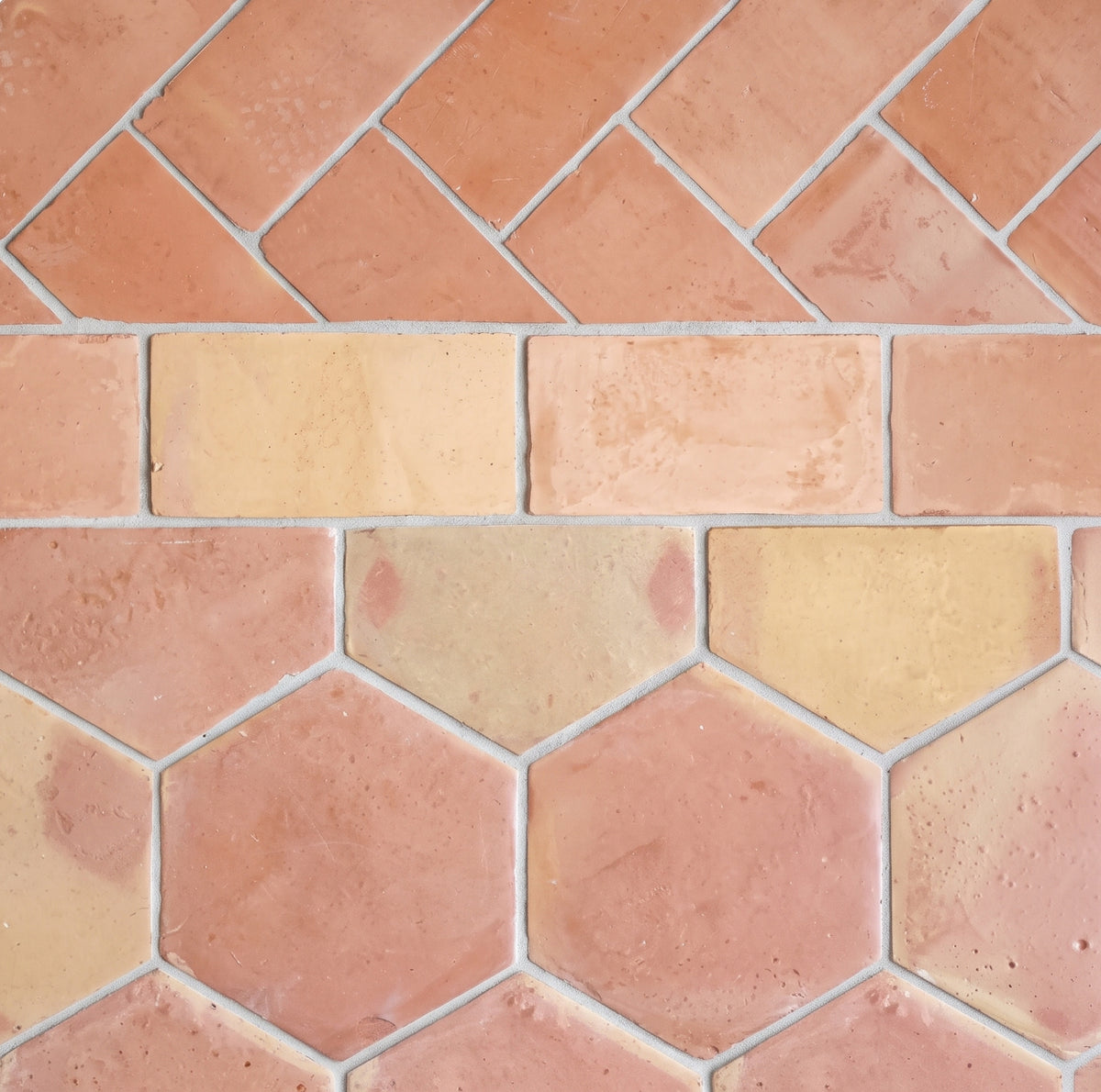 Terracotta and beige hexagonal tiles arranged in a herringbone and brick pattern, showing a textured clay finish with light gray grout lines.