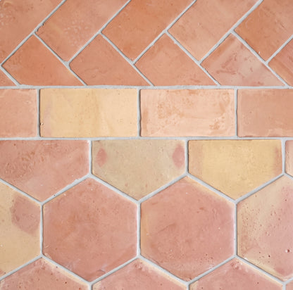 Terracotta and beige hexagonal tiles arranged in a herringbone and brick pattern, showing a textured clay finish with light gray grout lines.