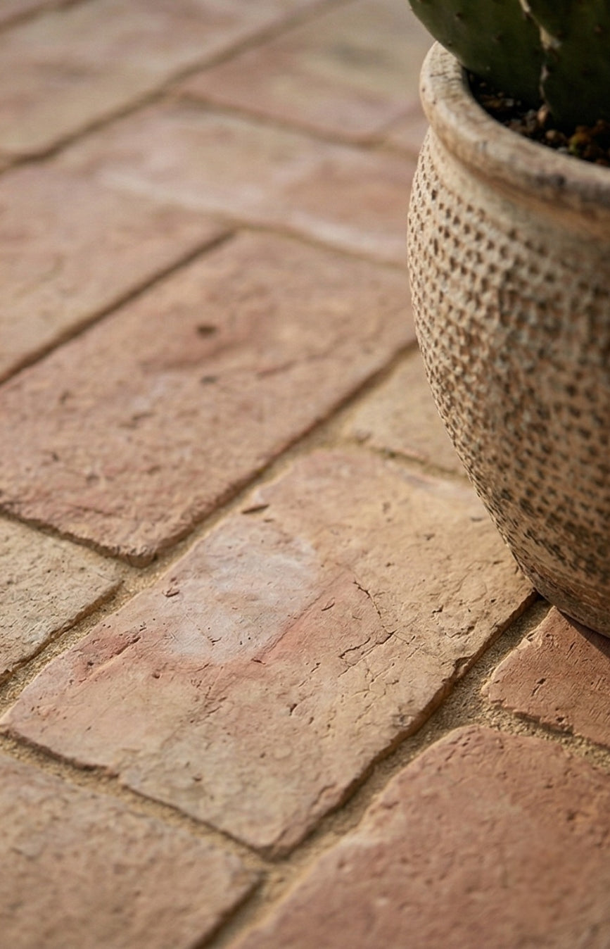 Terracotta rustic brick paver from Clay Imports Pavers, with an earthy textured surface and sandy grout, beside a decorative pot.