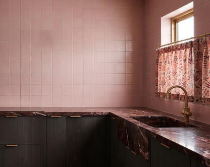 Modern kitchen with pink tiled walls and a window with floral curtains.