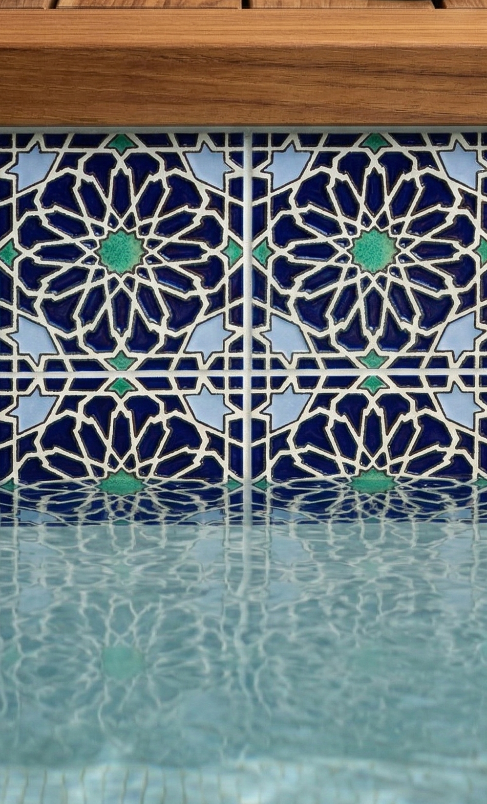 Deep blue Layla pattern tile with geometric stars and green accents, reflecting in rippled pool water below a wooden edge.