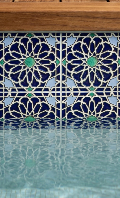 Deep blue Layla pattern tile with geometric stars and green accents, reflecting in rippled pool water below a wooden edge.
