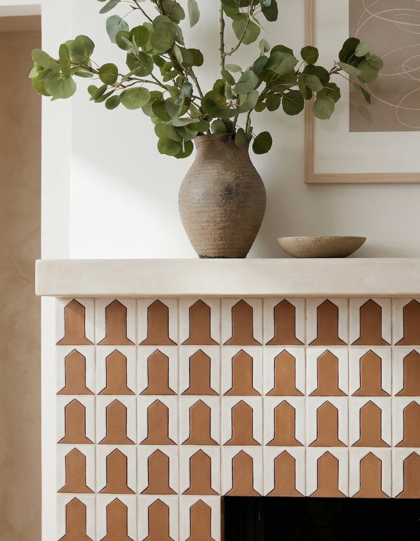Terracotta and cream geometric tiles by Clay Imports, with a repeated bell-shaped pattern on a white fireplace.