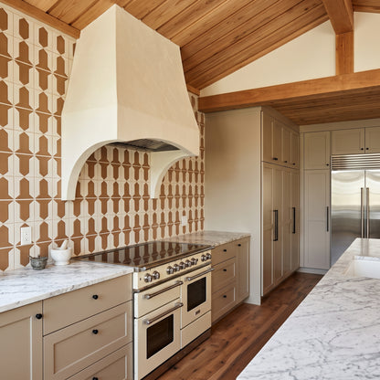 A modern kitchen features a cream-colored range beneath a custom plaster hood, set against a backdrop of geometric brown and white tile.