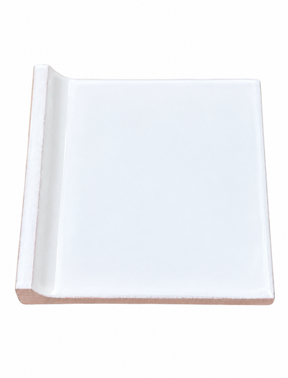 A glossy white ceramic tile features a raised bullnose edge on one side and a terracotta base.