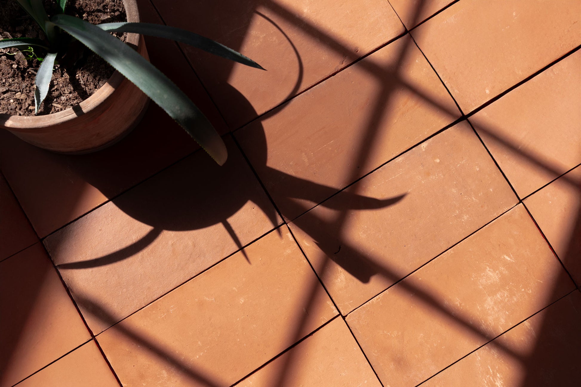 Baked Thin Terracotta Paver by Clay Imports, warm reddish-brown tiles showcasing geometric shadows.